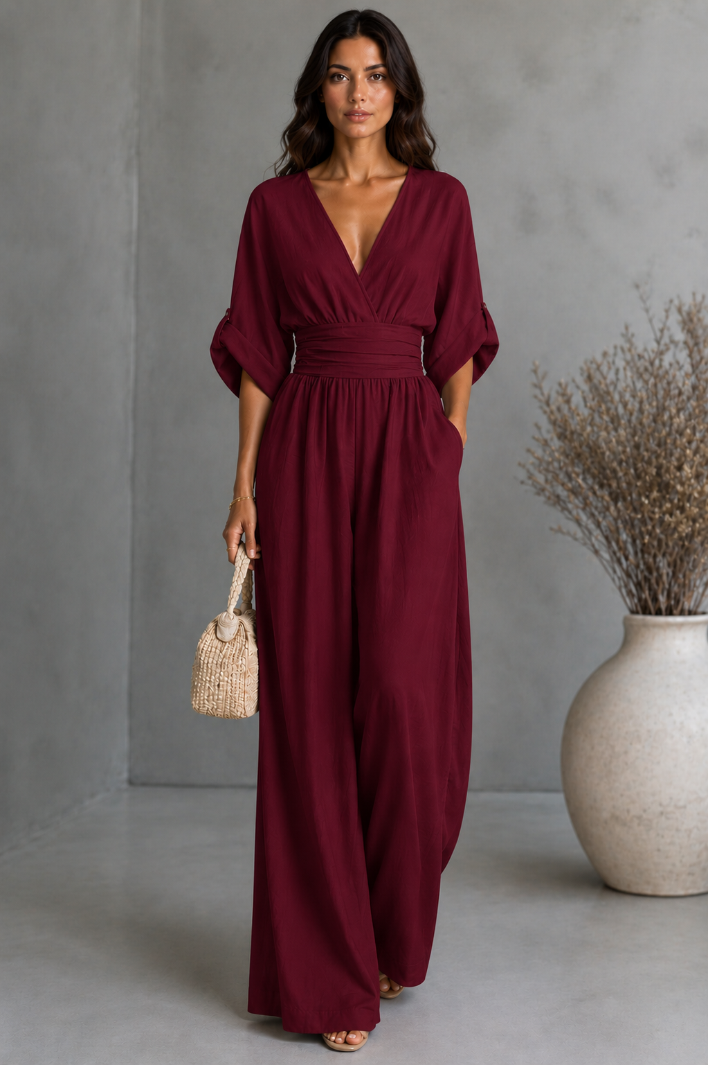 Woman wearing a burgundy dress holding a woven handbag against a gray background