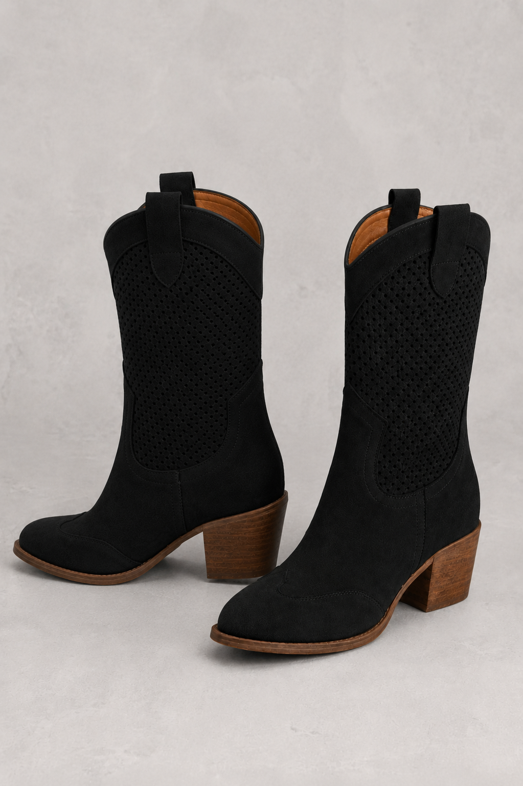 Black cowboy boots with brown soles on a light gray background