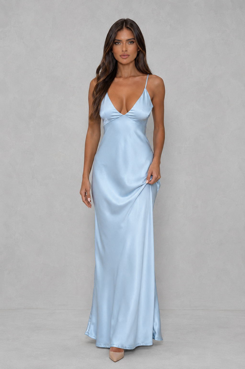 A woman modeling a light blue satin slip maxi dress with spaghetti straps and a sweetheart neckline, standing against a neutral gray studio backdrop.