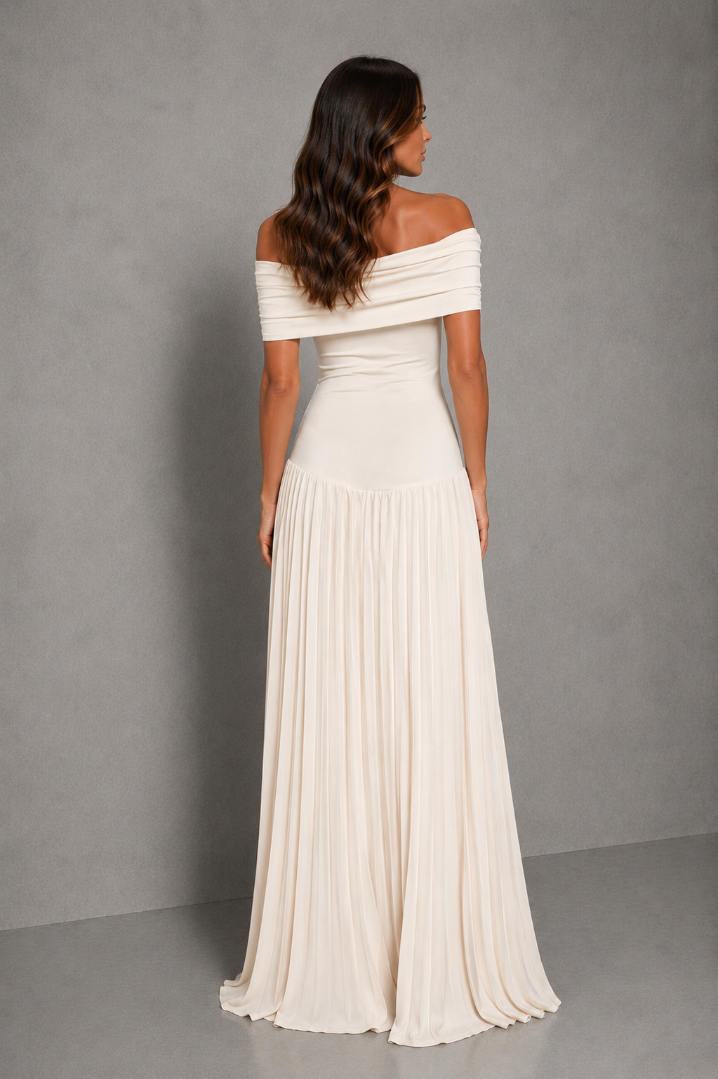 An off-the-shoulder floor-length pleated gown in a warm off-white or cream color, shown from the back on a model against a gray studio backdrop.