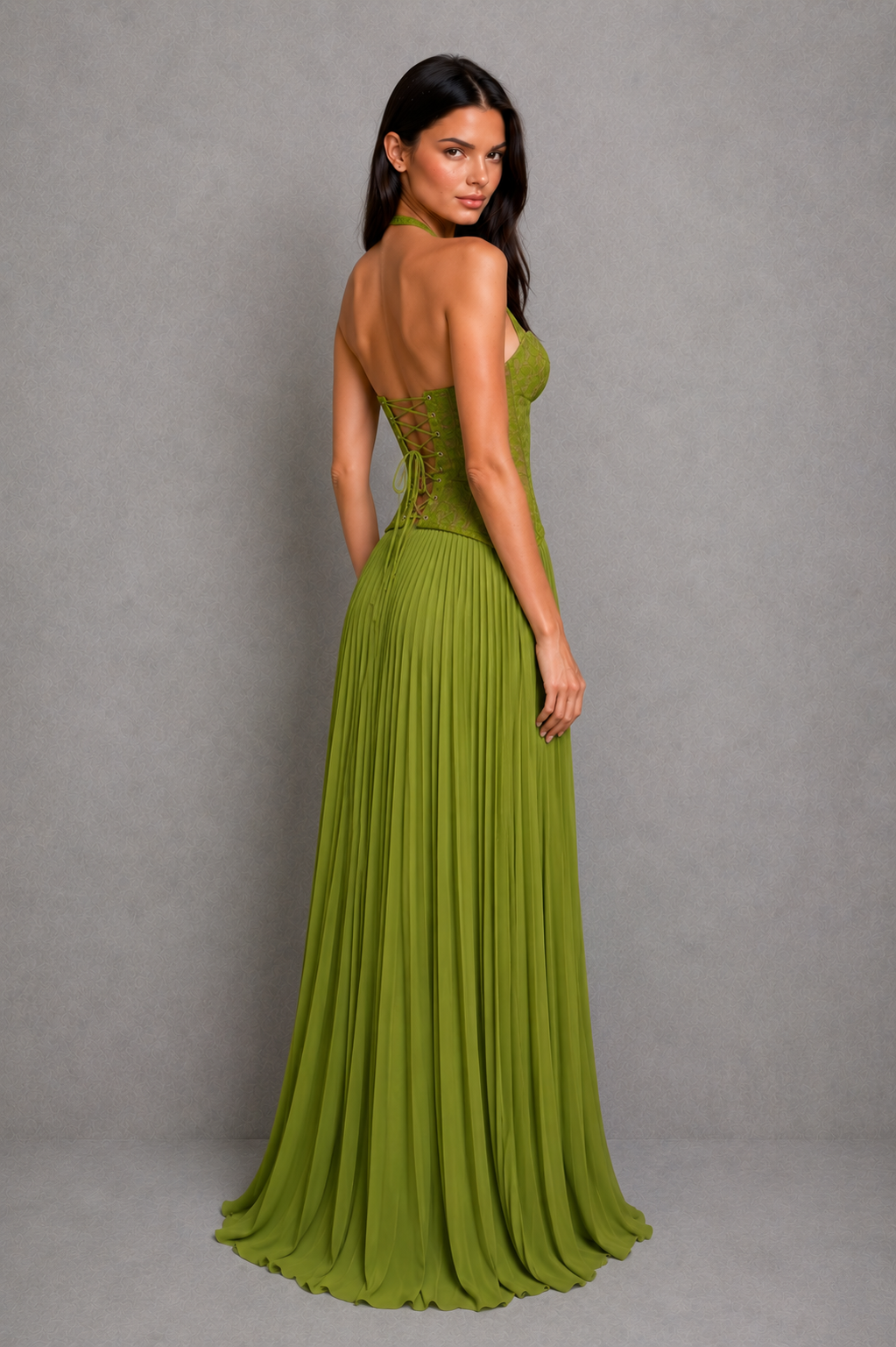 Woman wearing a green evening gown with a pleated skirt against a gray background
