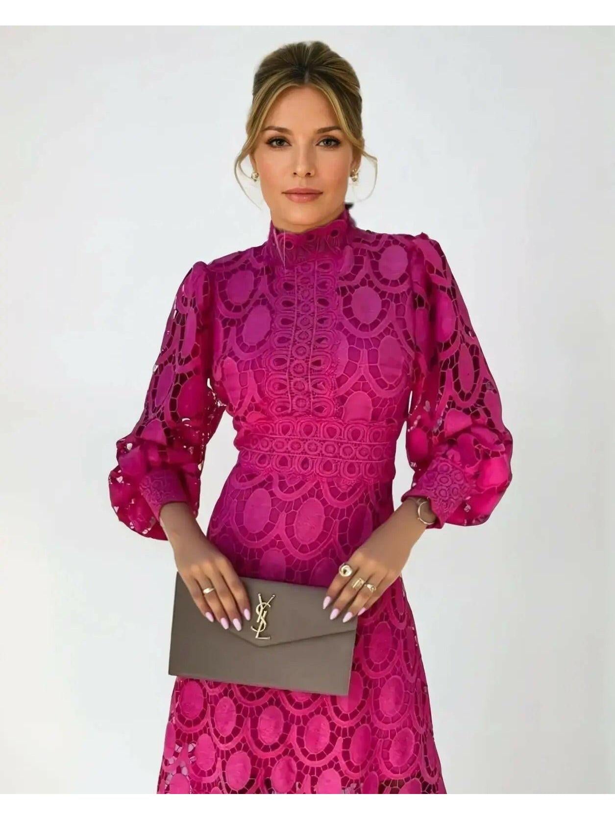 Woman wearing a pink lace dress holding a YSL handbag against a white background