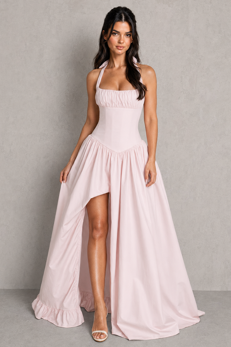 Woman wearing a light pink halter neck dress with a high-low hem on a gray background
