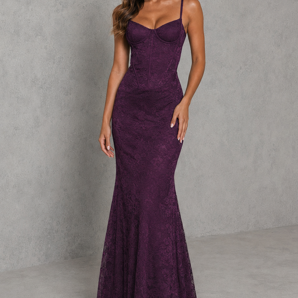 A woman modeling a sleeveless, fitted mermaid-style gown in deep plum purple lace, standing against a textured gray studio backdrop.