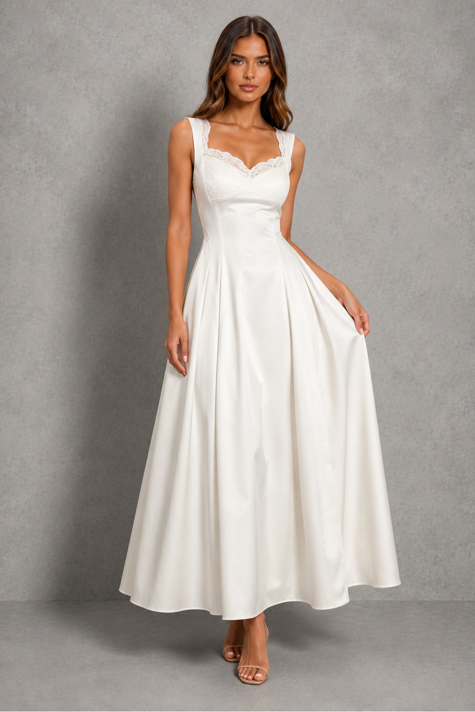 A woman modeling a sleeveless white maxi dress with a sweetheart neckline, lace trim, and a full satin skirt, standing against a textured gray studio backdrop.