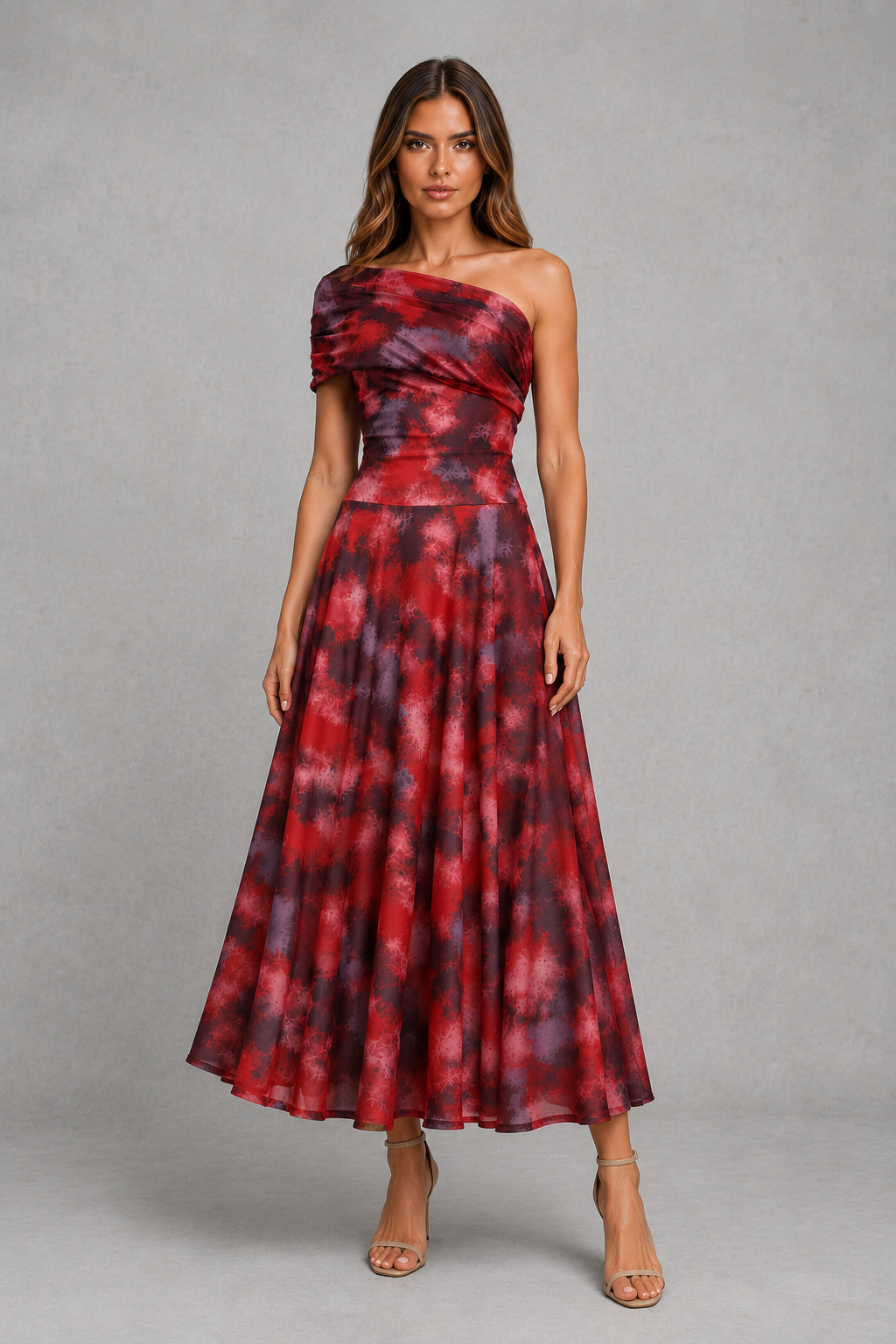A woman modeling a one-shoulder midi dress with a red and purple tie-dye pattern, standing against a neutral gray studio background.
