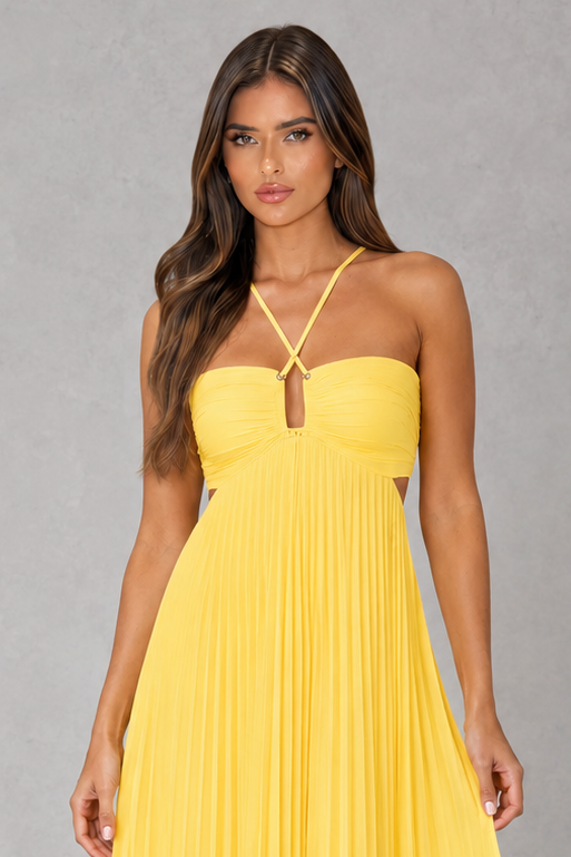 A woman modeling a bright yellow strapless maxi dress with a sweetheart neckline, thin crisscross halter straps, and a pleated skirt, set against a neutral gray studio background.