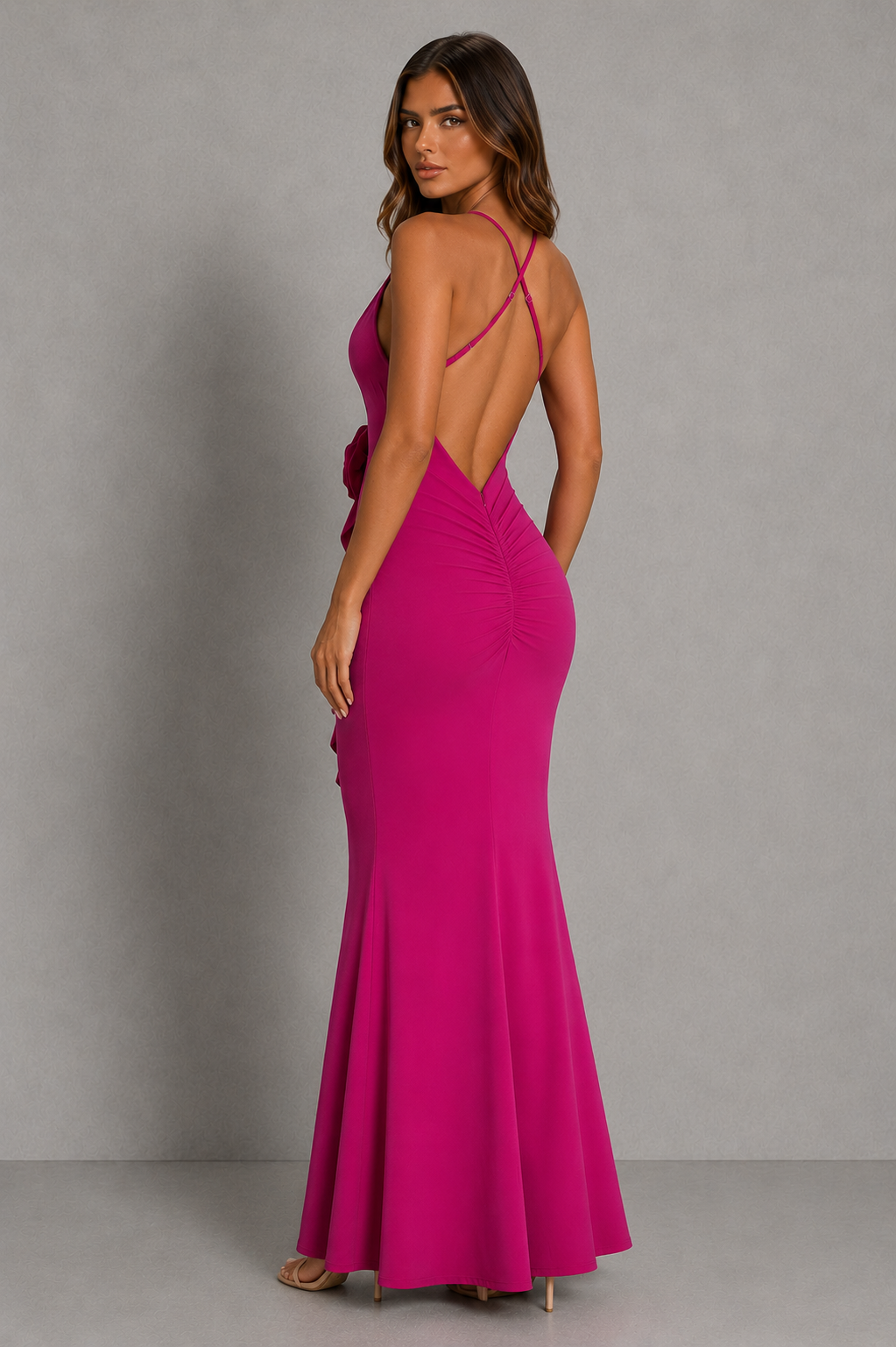 Woman wearing a vibrant pink evening gown with a backless design against a gray background