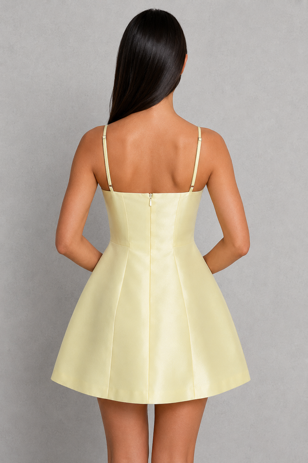 Woman wearing a light yellow dress with thin straps on a gray background