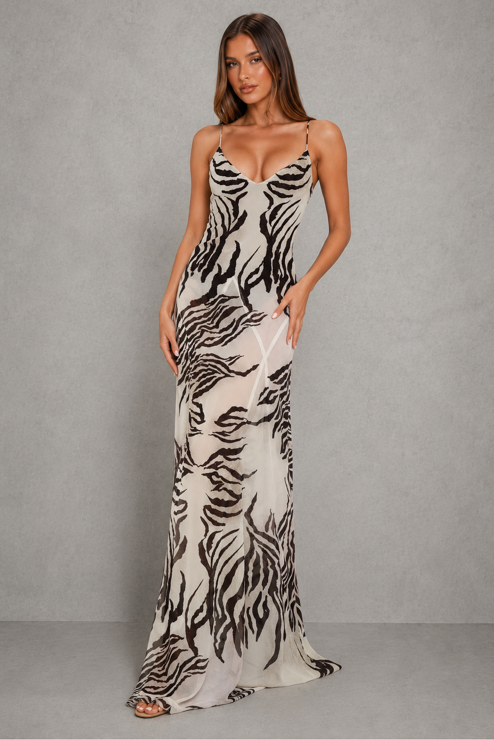 A woman modeling a floor-length slip gown with a black and off-white zebra print against a textured gray studio backdrop.