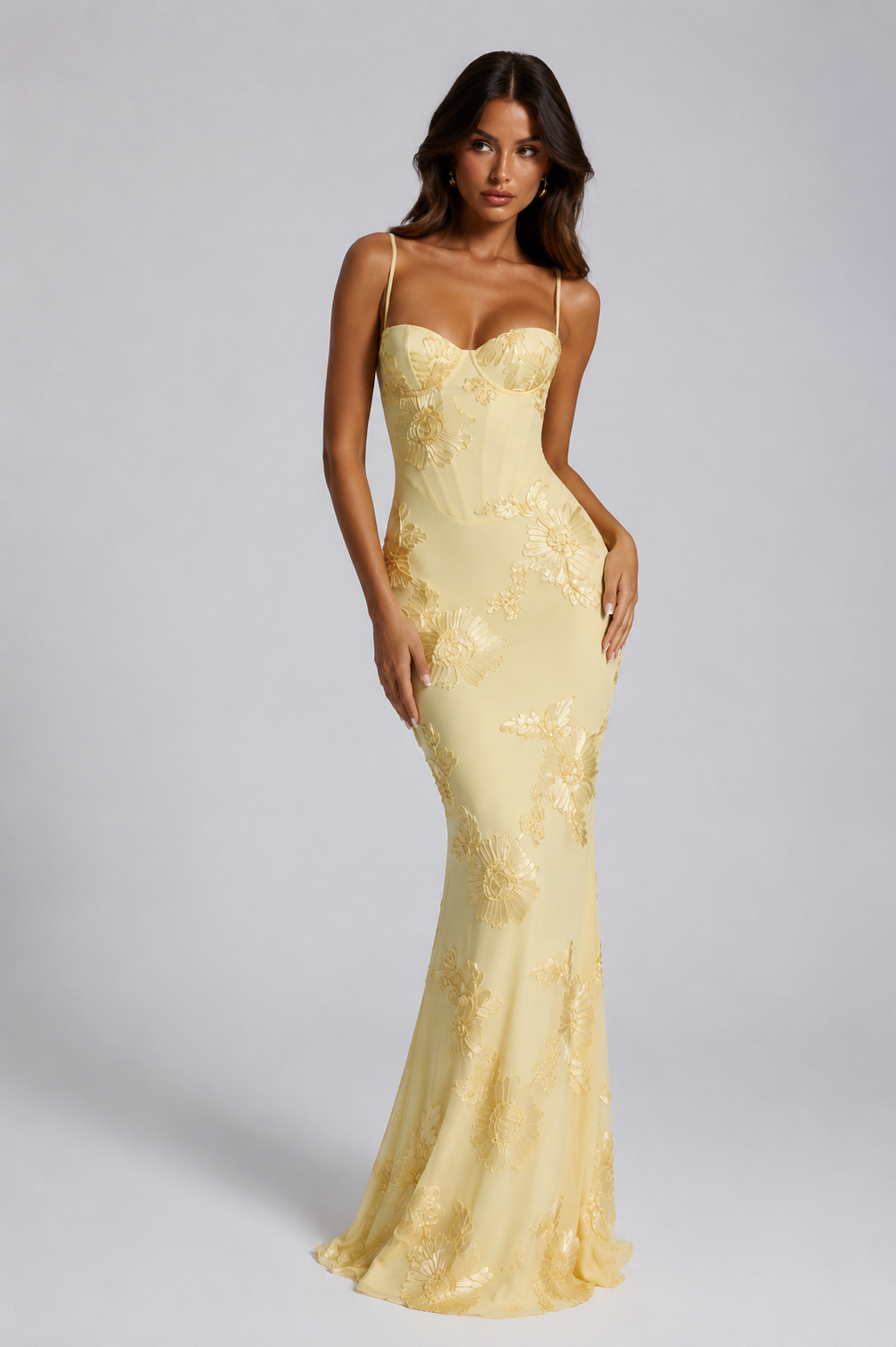 Woman wearing a yellow evening gown with floral details on a gray background