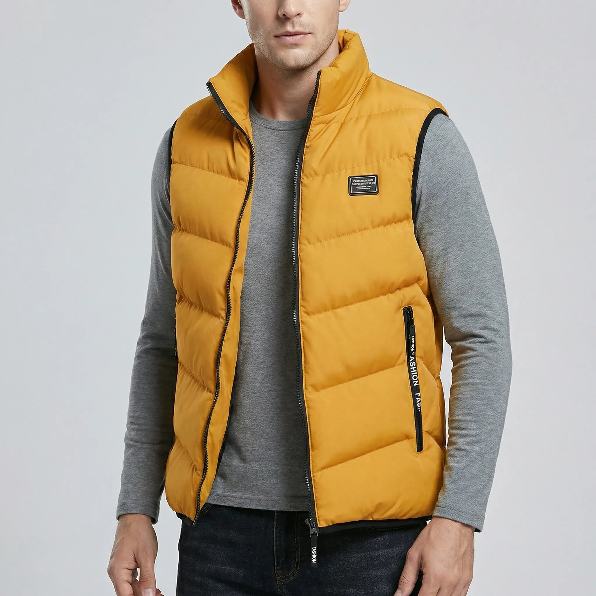 Man wearing a mustard yellow puffer vest over a gray shirt on a light gray background