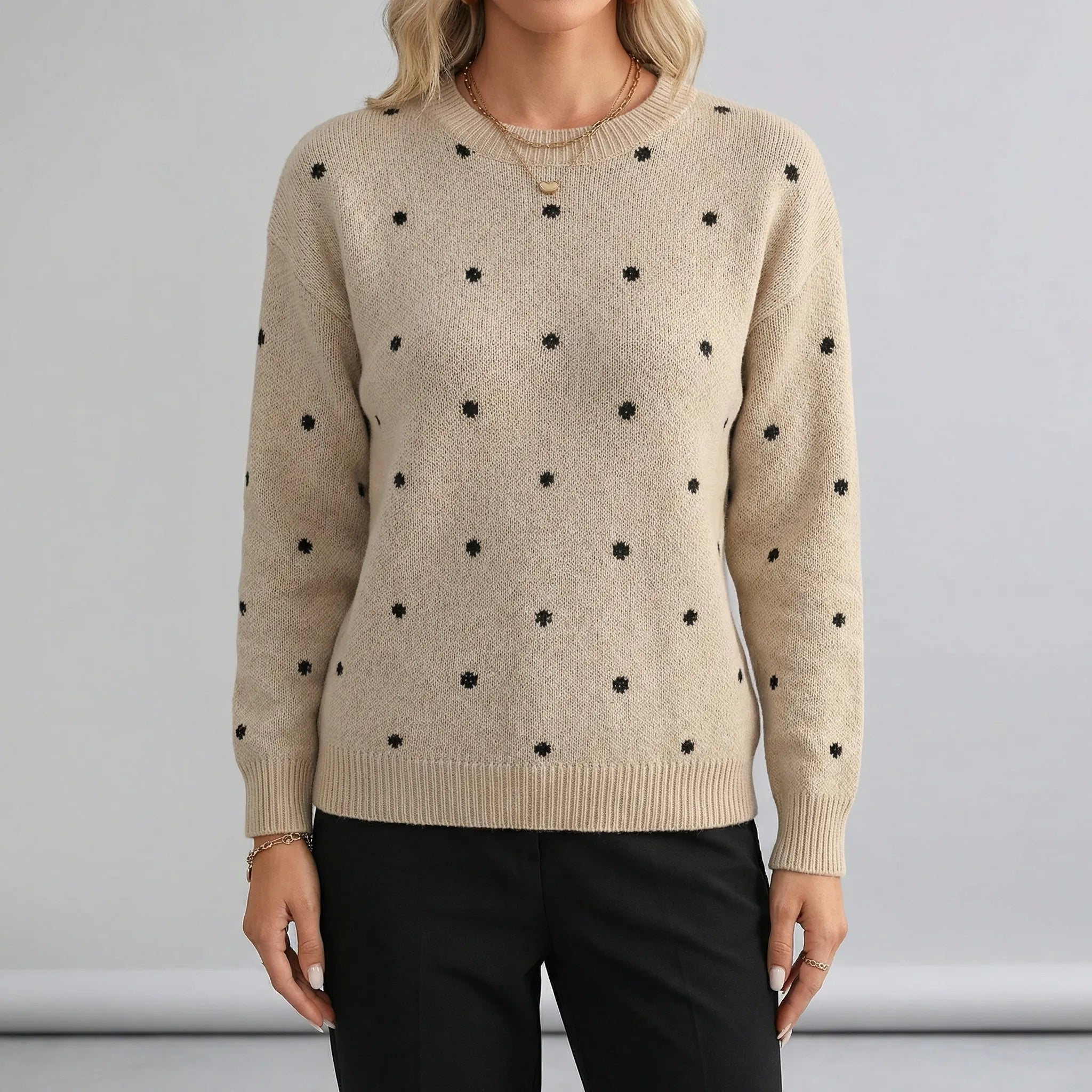 Beige sweater with black polka dots worn by a person on a gray background