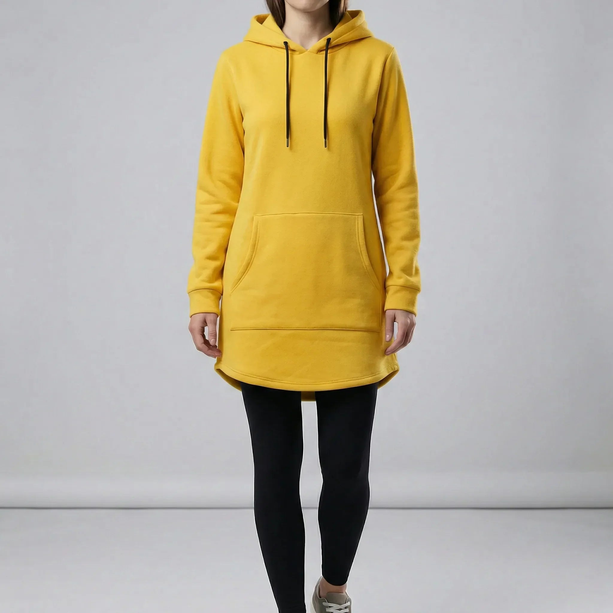 Person wearing a yellow hoodie and black leggings on a plain background