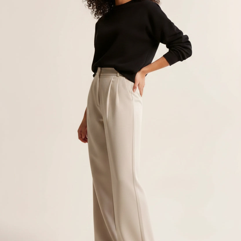 Woman wearing a black sweater and beige pants on a plain background