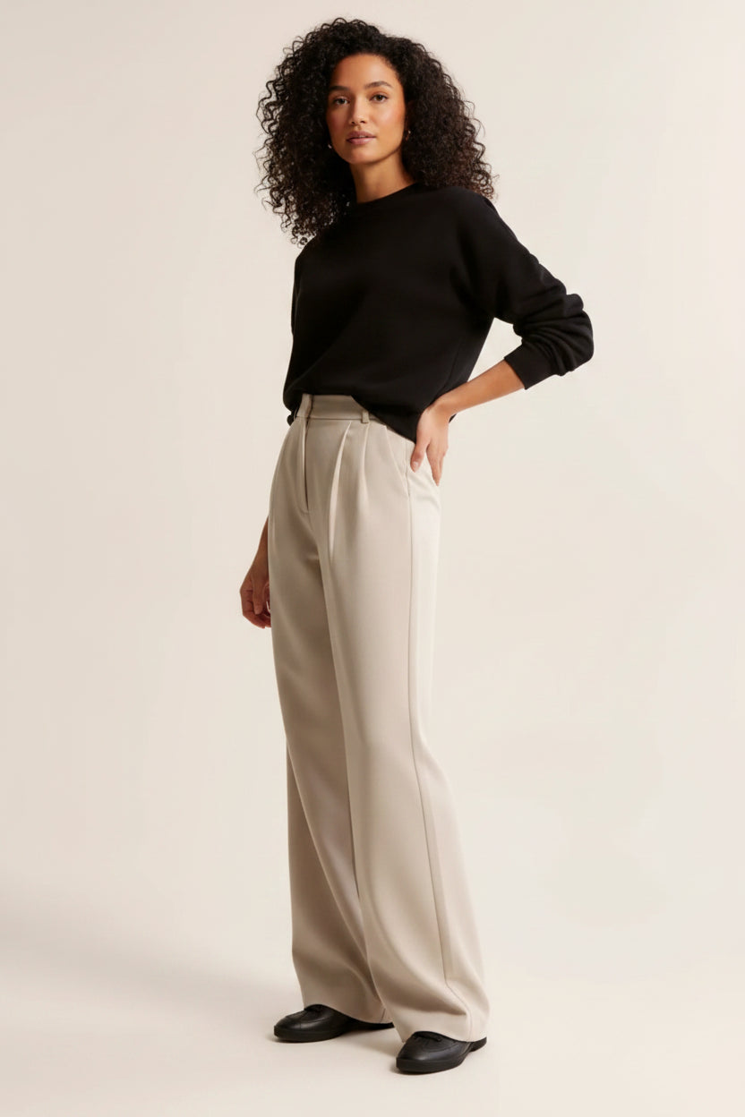 Woman wearing a black sweater and beige pants on a plain background