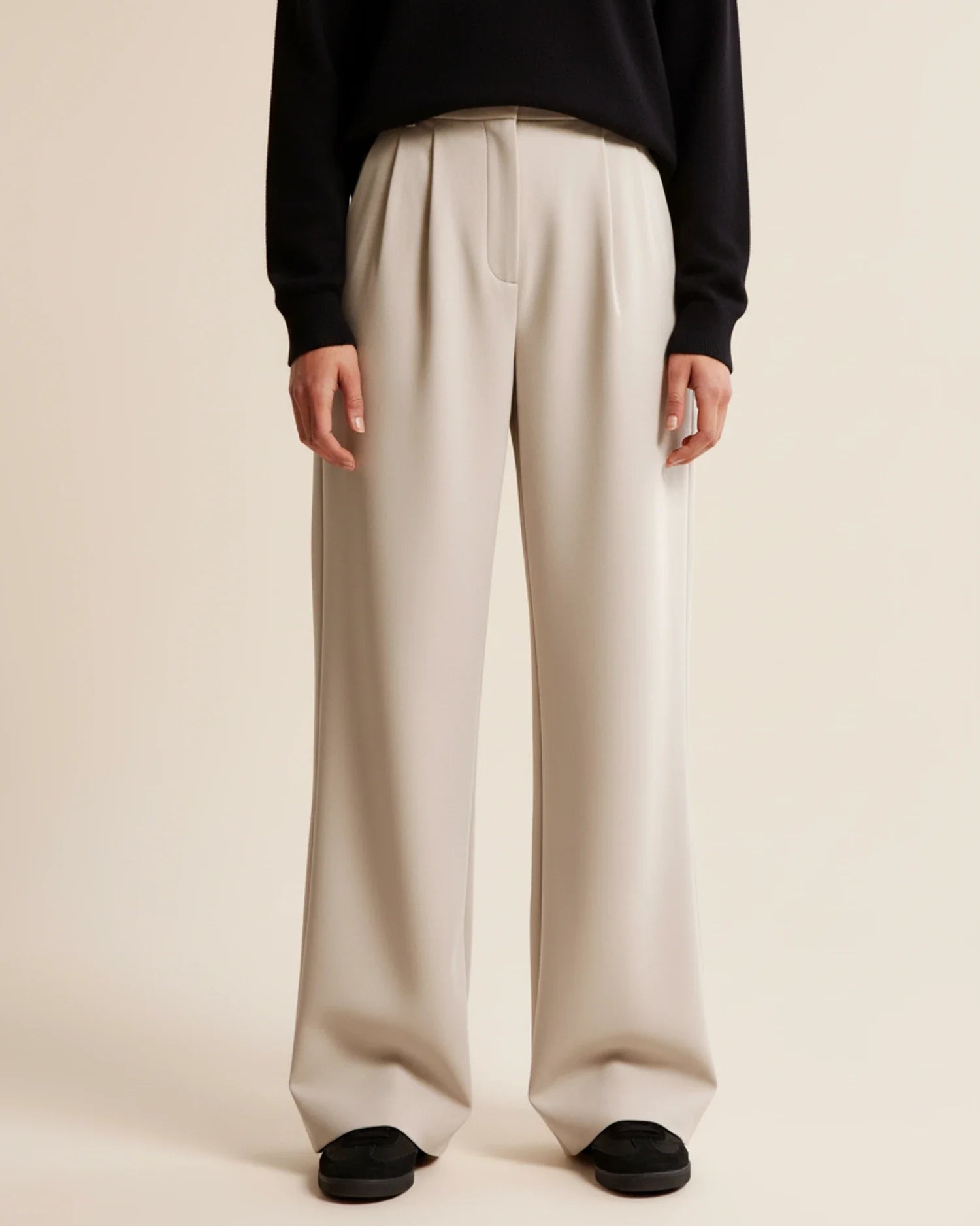 Person wearing beige wide-leg pants and a black top on a plain background