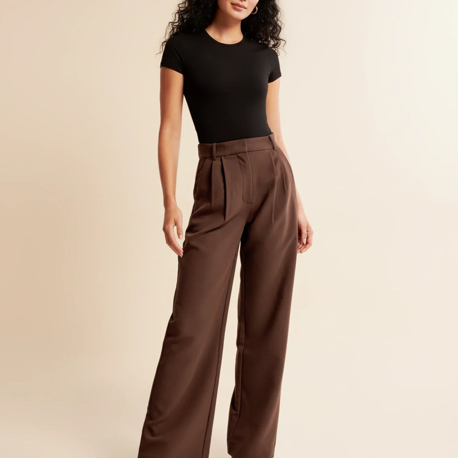Woman wearing a black top and brown wide-leg pants on a beige background