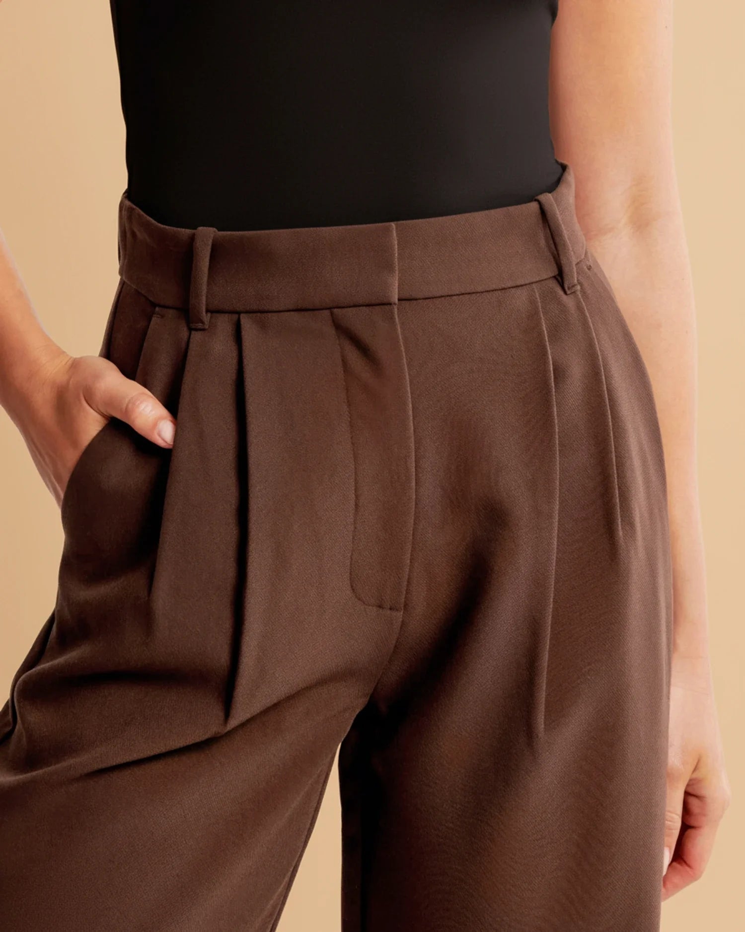 Brown pleated pants worn by a person on a beige background