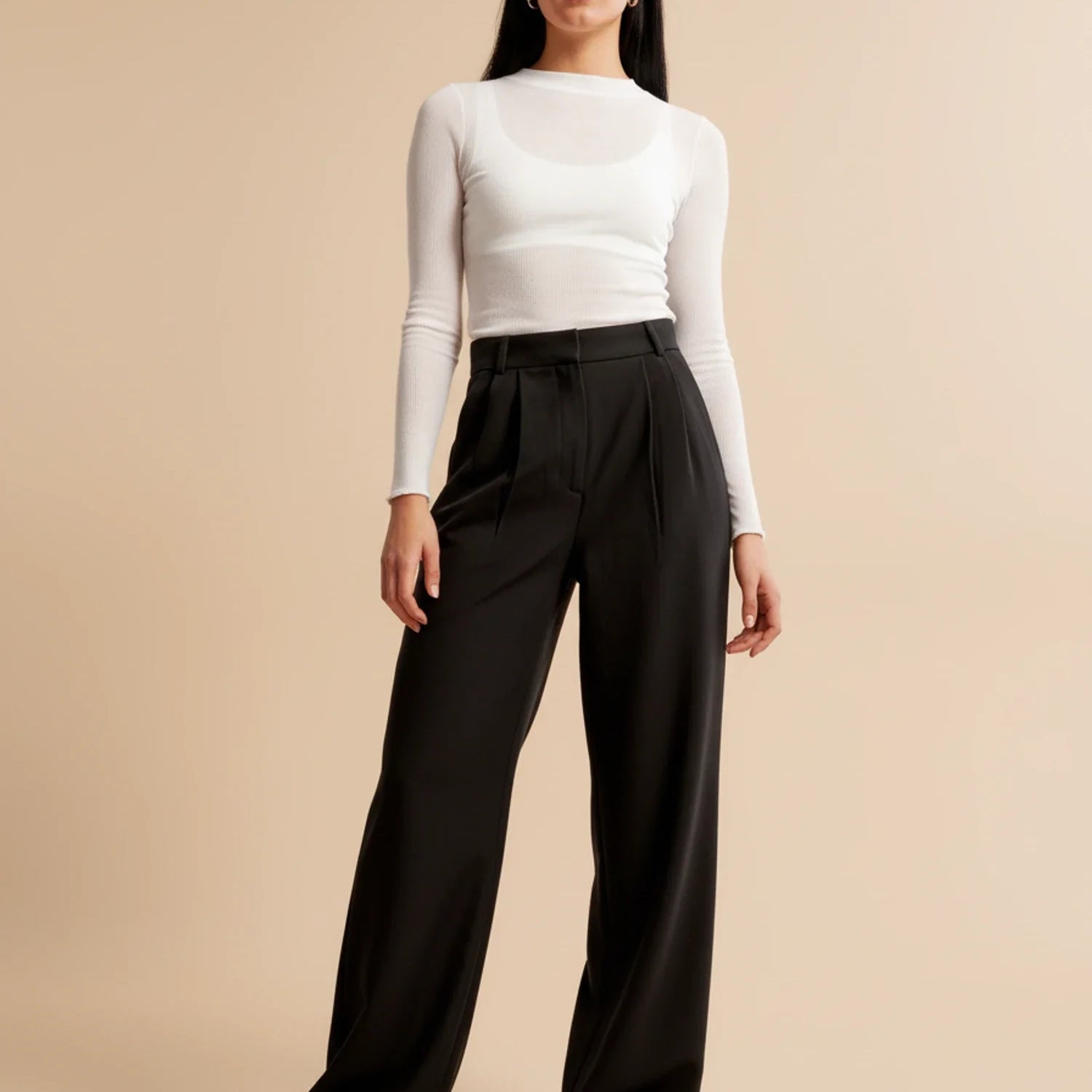Woman wearing a white long-sleeve top and black wide-leg pants on a beige background