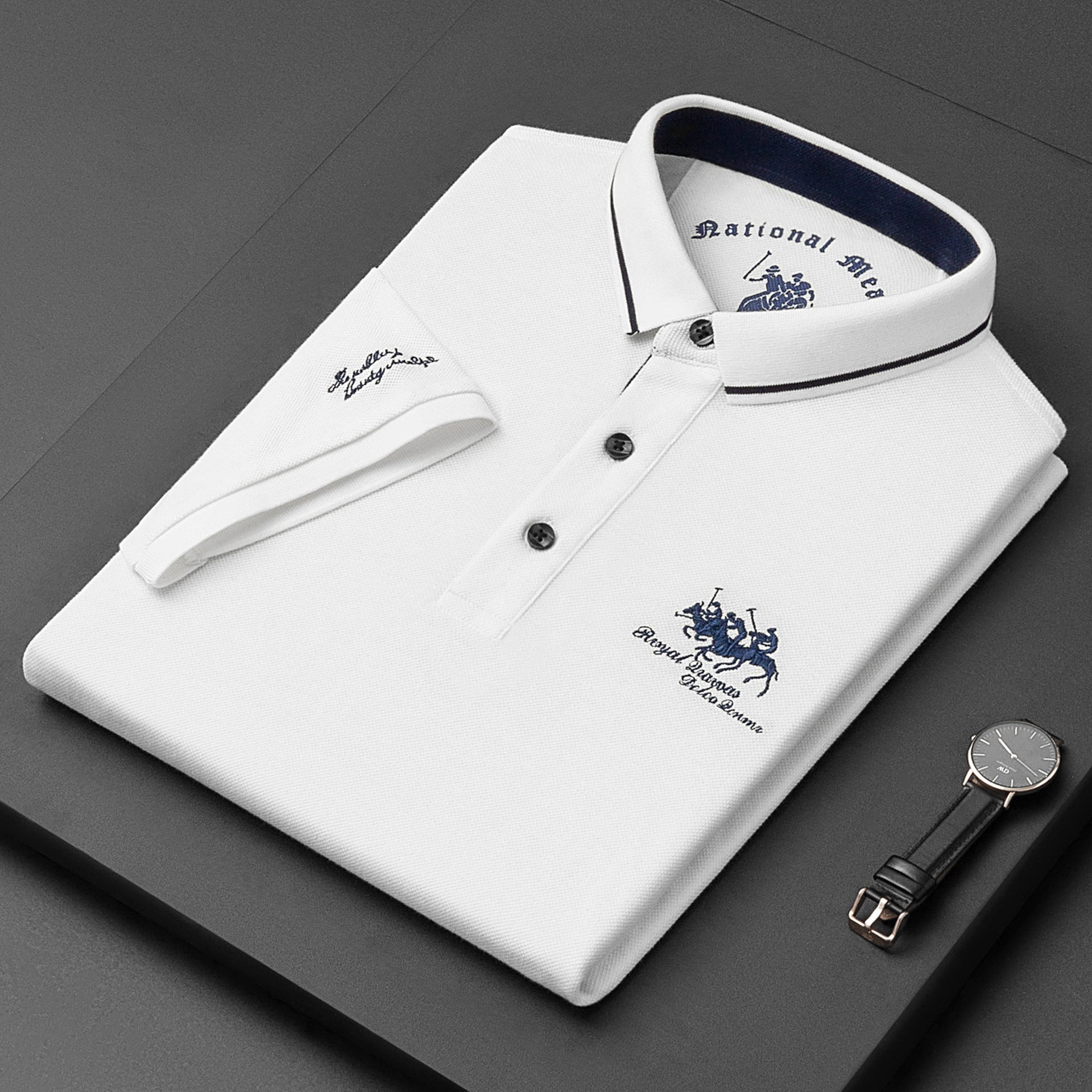 White polo shirt with brand logos on a dark surface, accompanied by a watch.