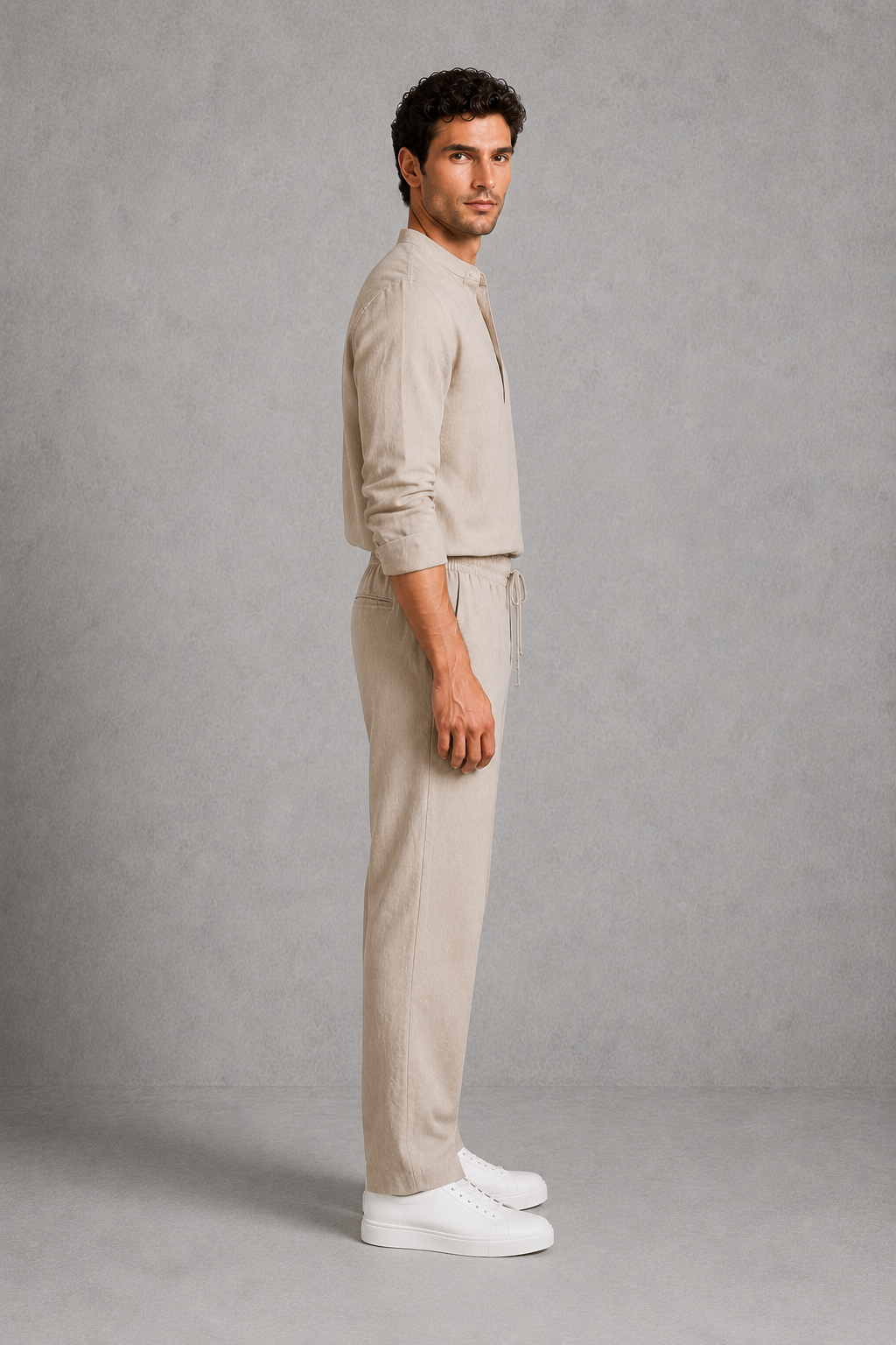 Man wearing a beige outfit standing against a gray background
