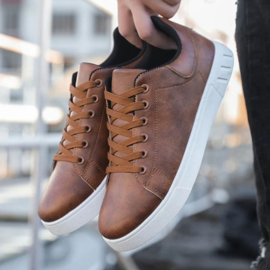 Brown leather sneakers with white soles held by a person against a blurred background