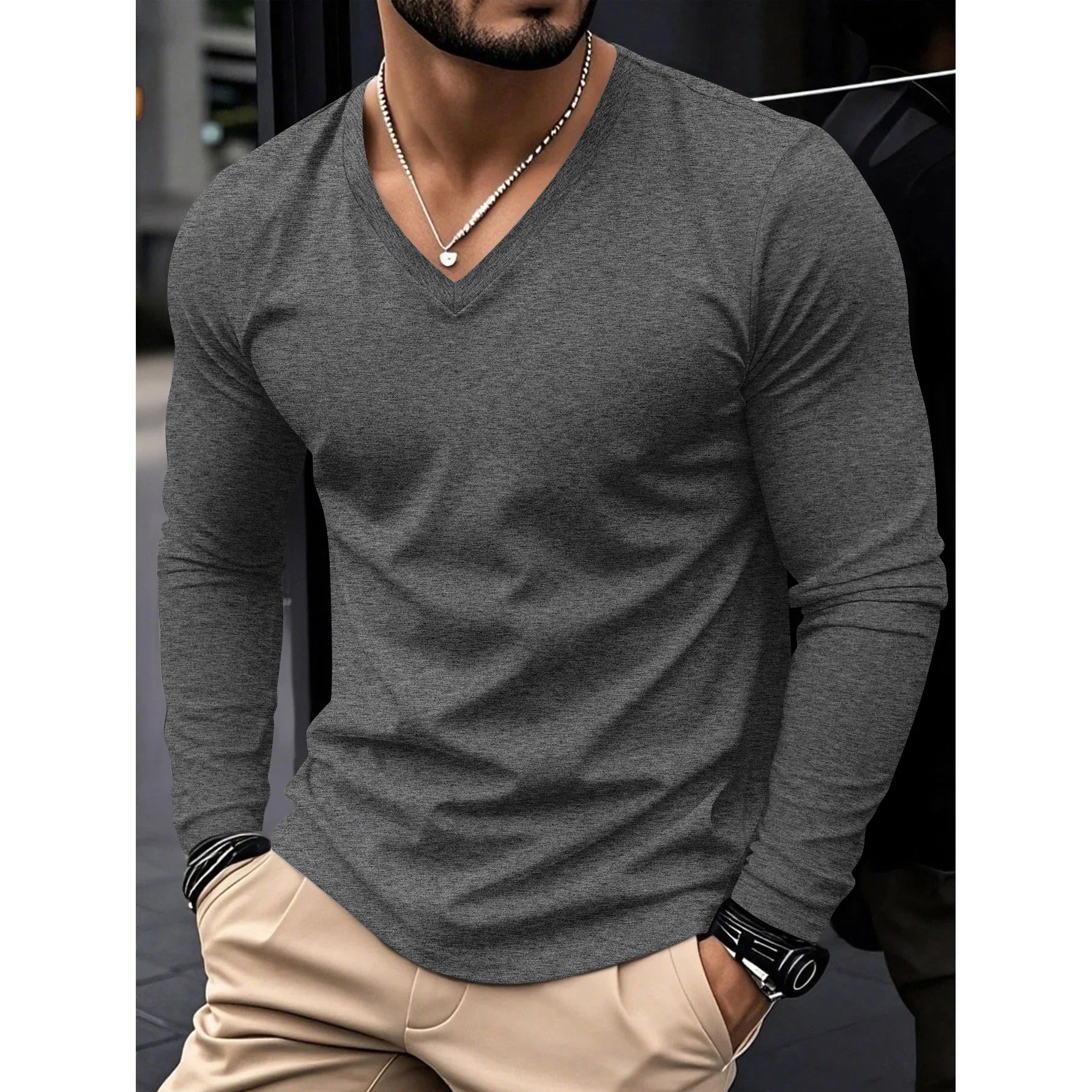 Man wearing a gray long-sleeve shirt with beige pants, standing against a blurred background.