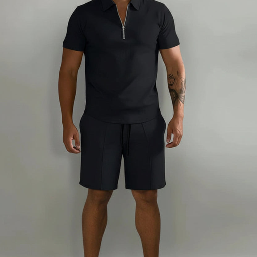 Person wearing a black polo shirt and shorts with white sneakers on a gray background