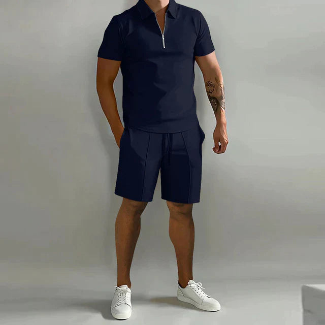 Person wearing a black polo shirt and shorts with white sneakers on a gray background