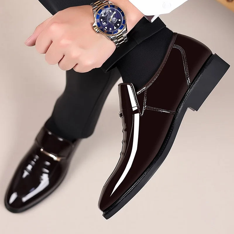 Black shiny dress shoes worn with black pants and a watch on a neutral background