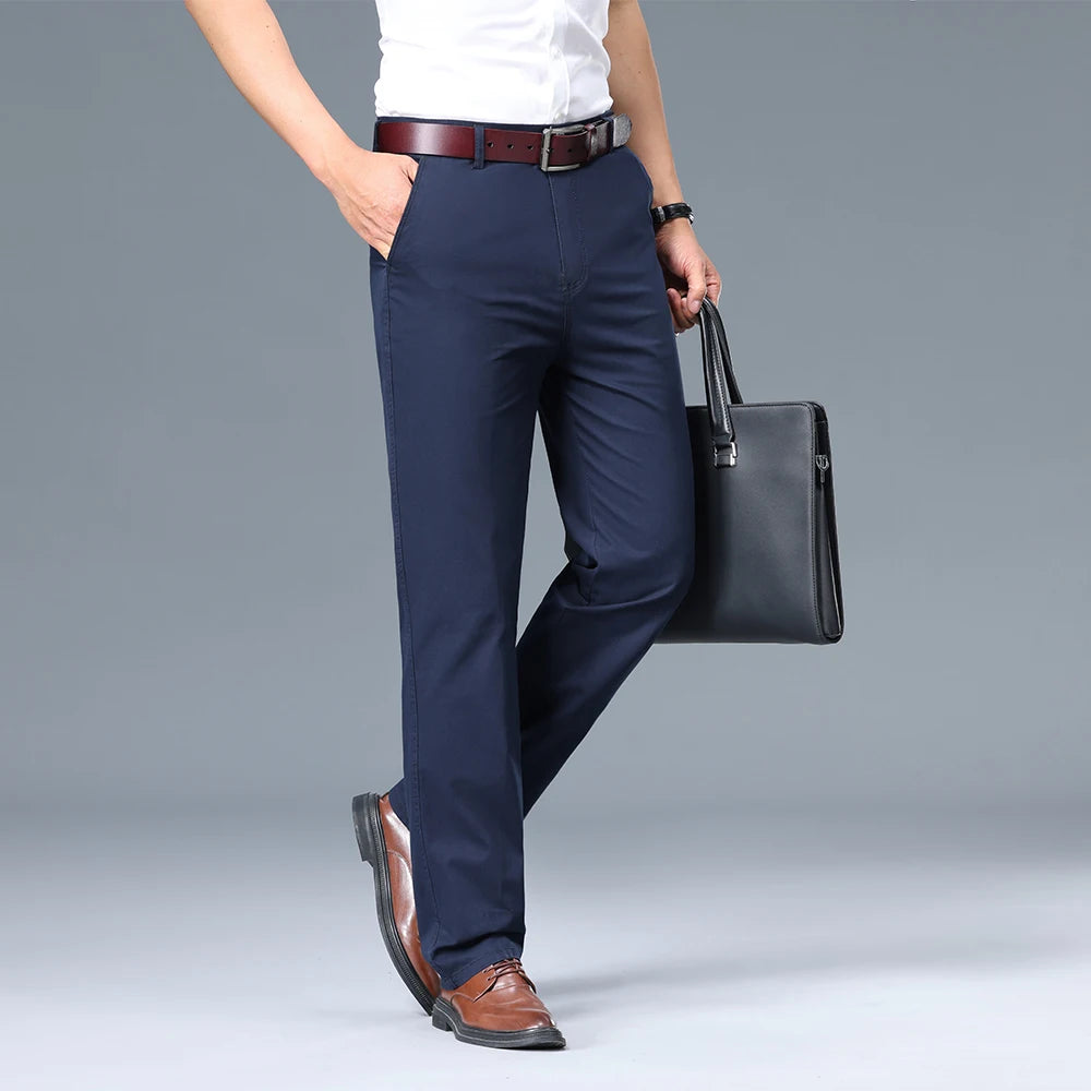 Person wearing navy pants with a white shirt, brown belt, and brown shoes, holding a black briefcase on a gray background.
