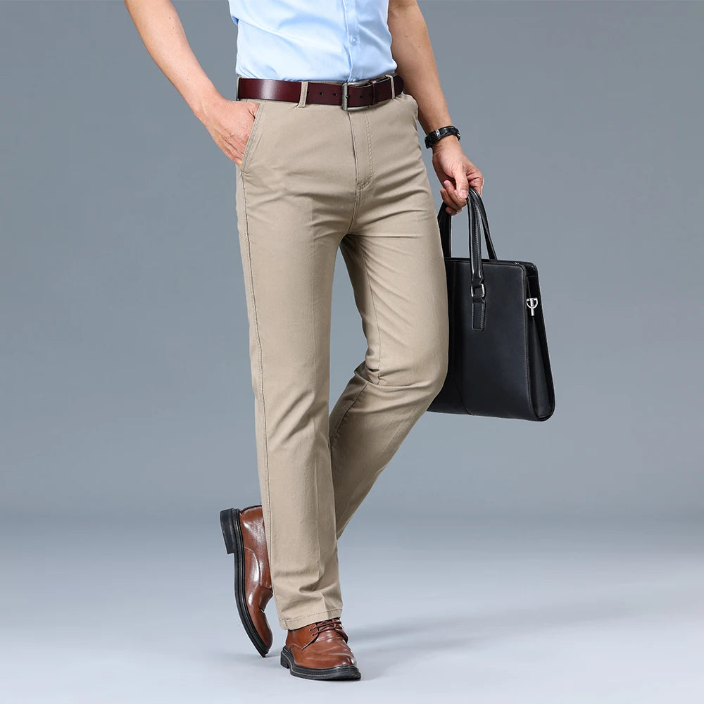 Person wearing beige pants, a light blue shirt, and brown shoes, holding a black briefcase on a gray background.