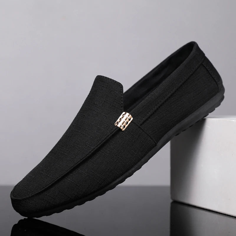 Black loafers with a gold buckle on a gray background