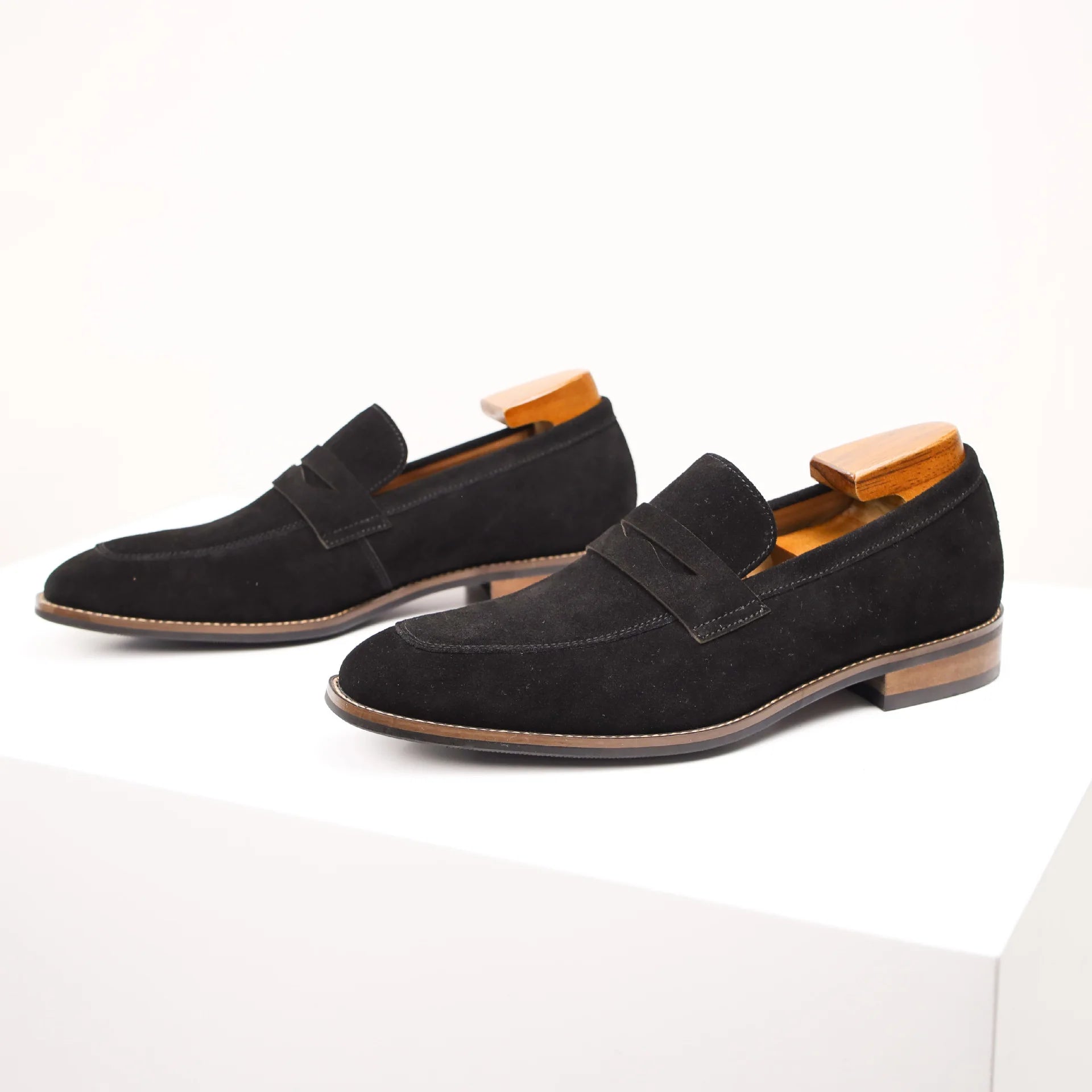 Pair of black suede loafers with wooden accents on a white background