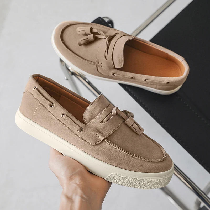 Pair of beige loafers with tassels held by a hand on a light gray background