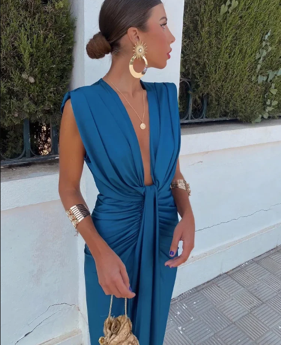 Woman wearing a blue dress with gold accessories outdoors.