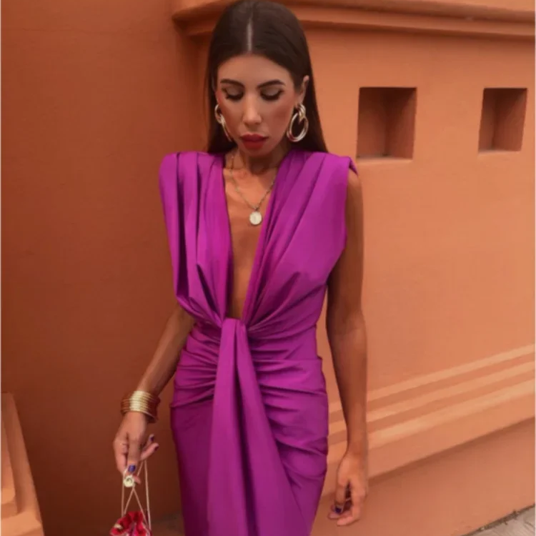 Woman in a vibrant purple dress standing against an orange wall.