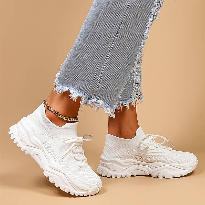 White sneakers worn with light blue jeans on a beige background