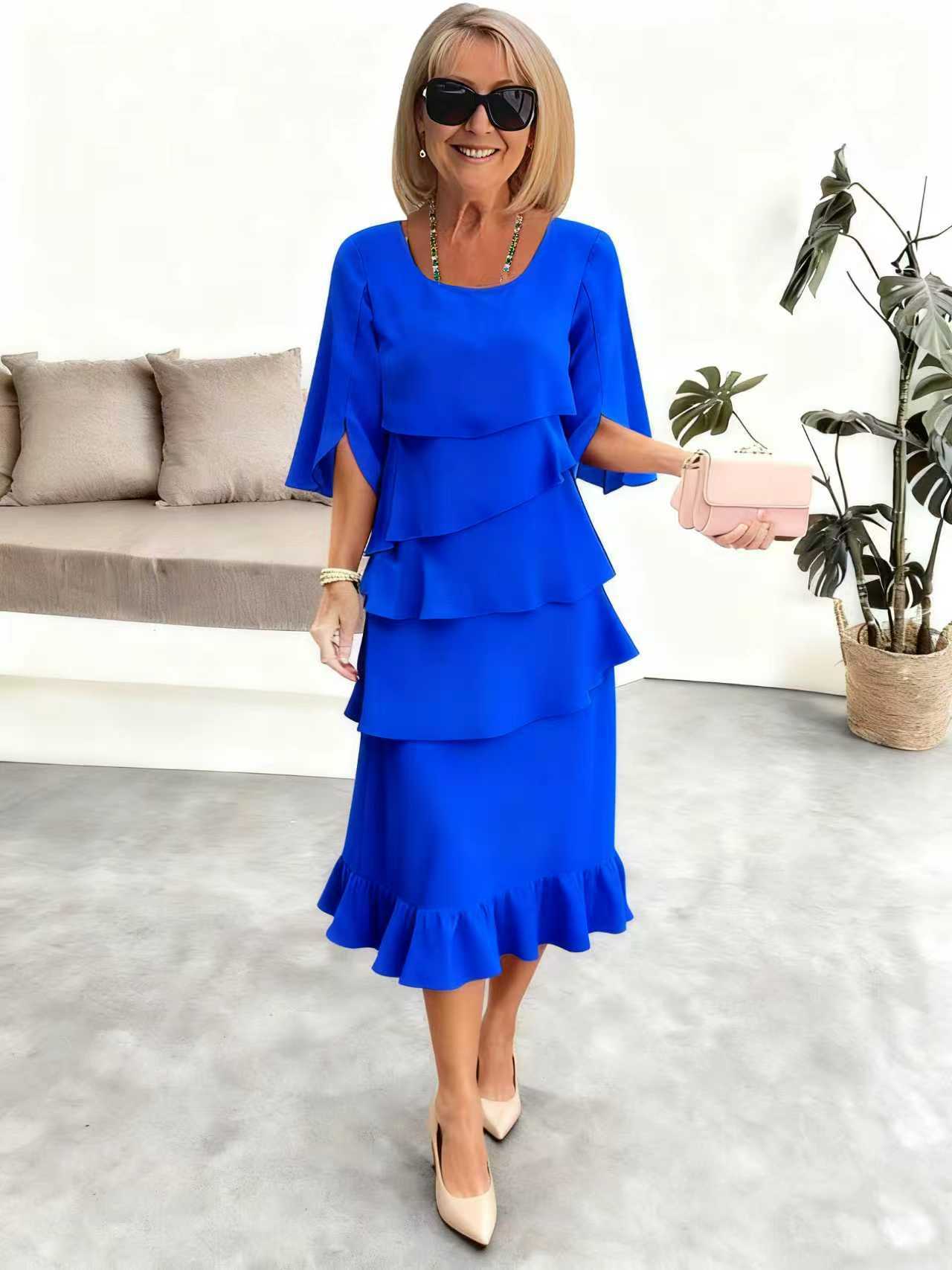 Woman wearing a blue dress in an indoor setting with a couch and plant in the background.