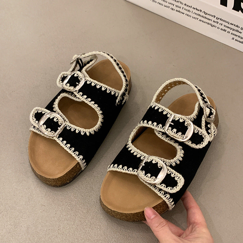 Black sandals with white lace details on a beige surface
