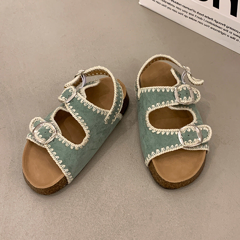 Pair of green sandals with white straps on a gray surface