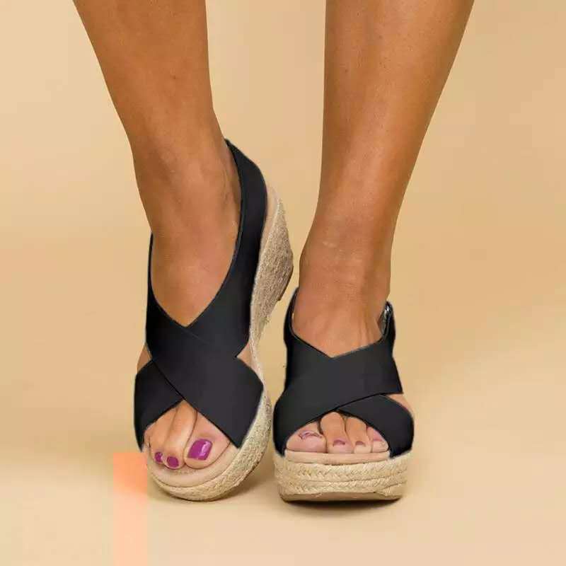 Black wedge sandals with espadrille sole worn by a person on a beige background