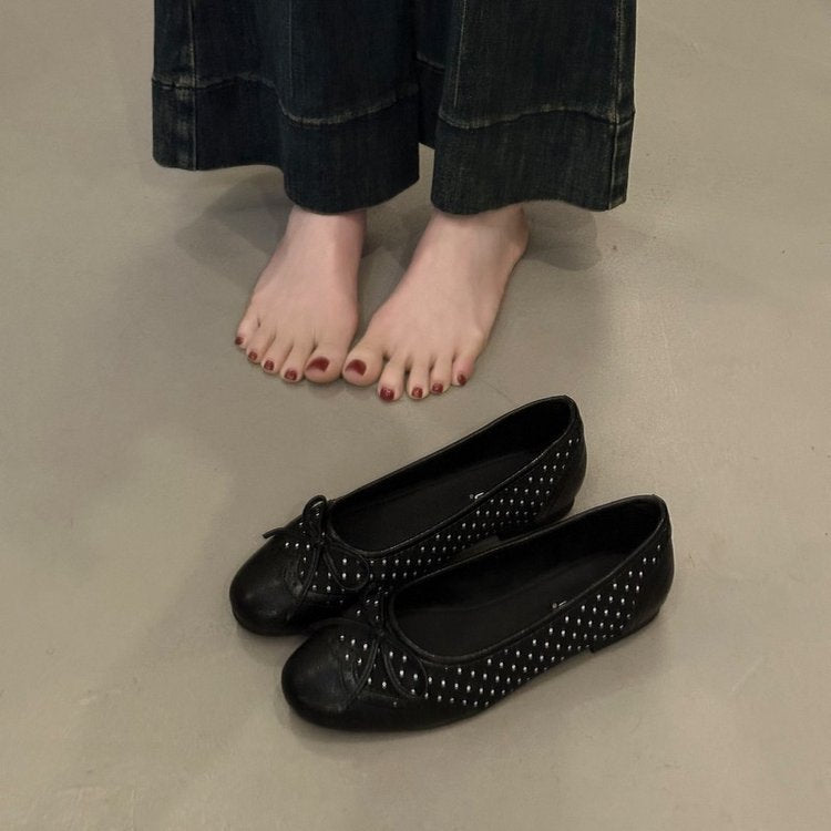 Black studded flats on a neutral floor with a person wearing black pants.