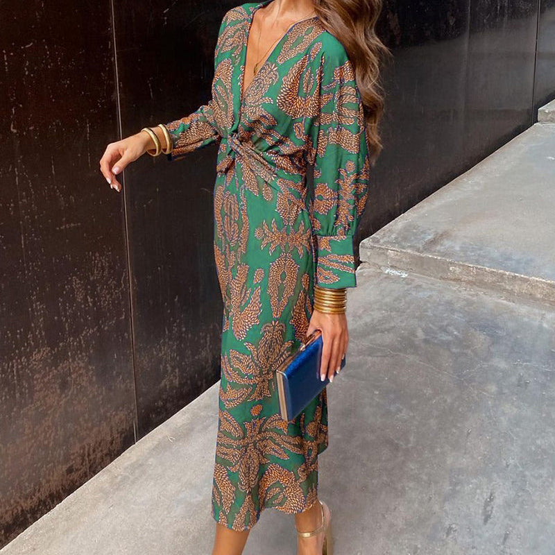 Woman in a green patterned dress standing against a black wall.