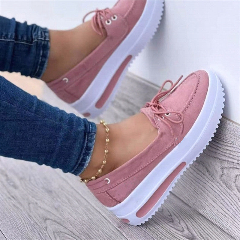 Pink platform shoes worn with blue jeans on a light wooden floor.