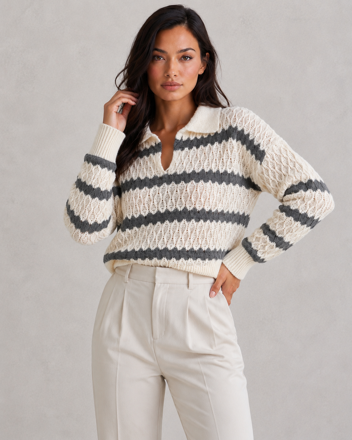 Woman wearing a striped sweater and white pants against a gray background
