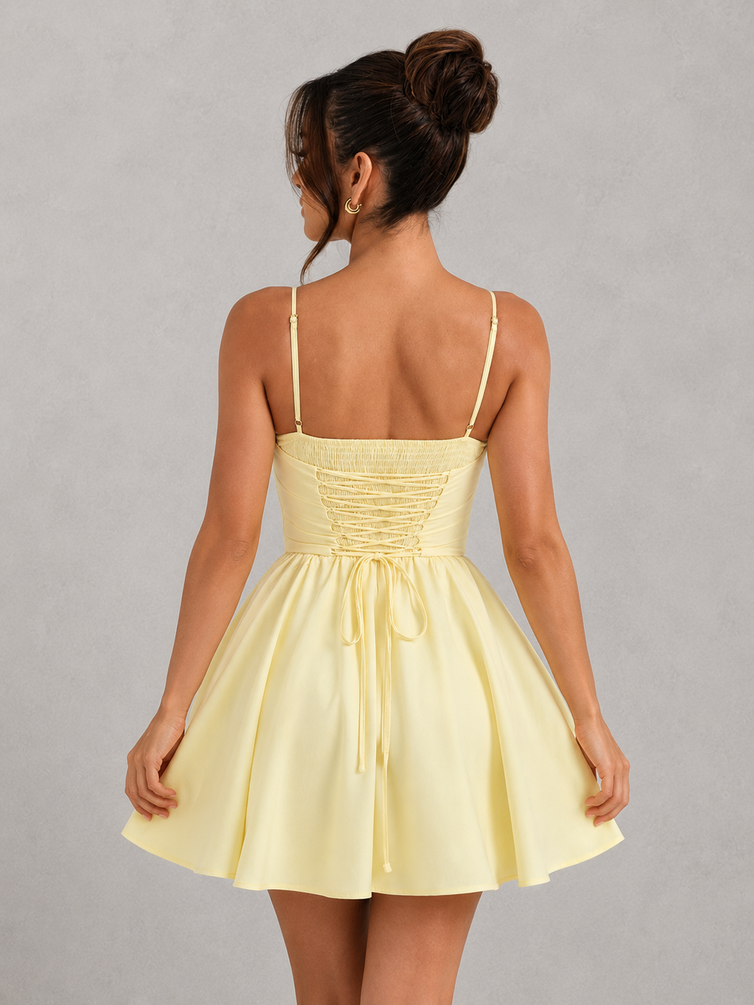 Woman wearing a yellow dress with thin straps on a gray background