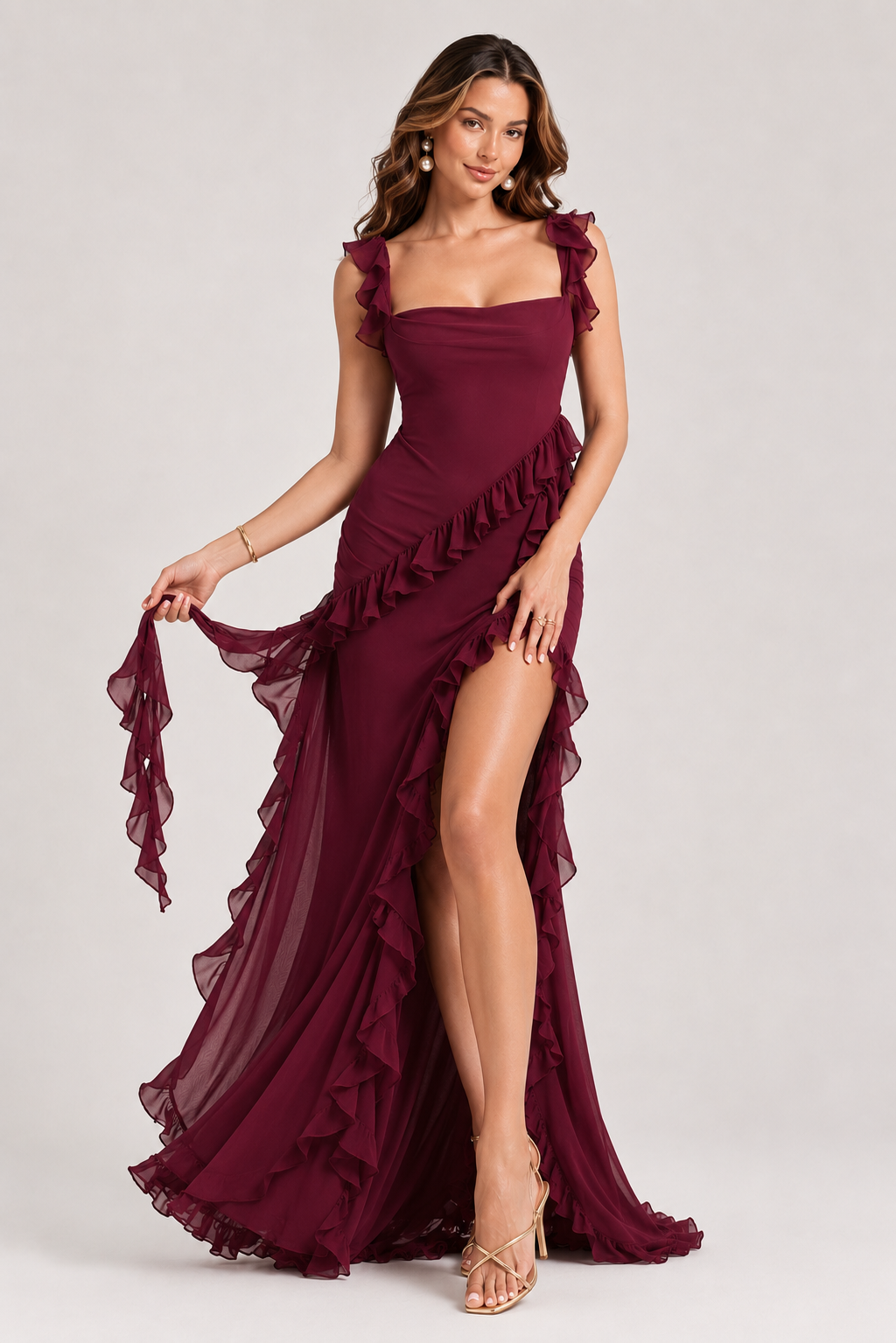 Woman wearing a burgundy evening gown with ruffled straps and a high slit on a white background