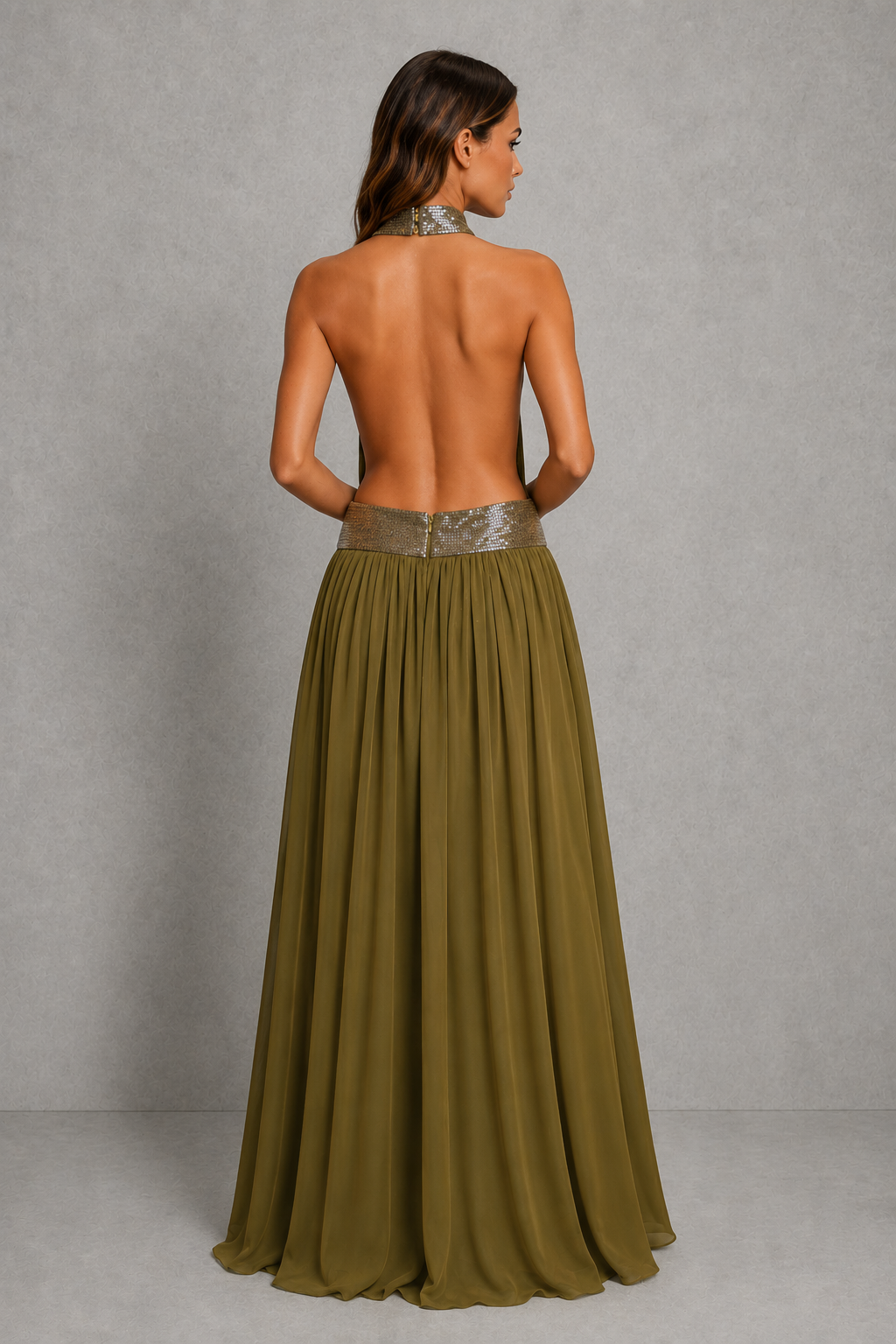 A woman shown from the back wearing a long, open-back olive green dress with a metallic silver patterned waistband, set against a textured gray studio background.